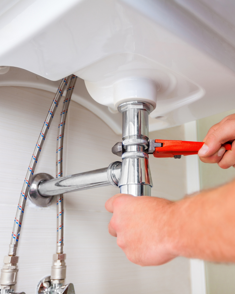 plumber tightening pipe under sink (800 x 1000 px)